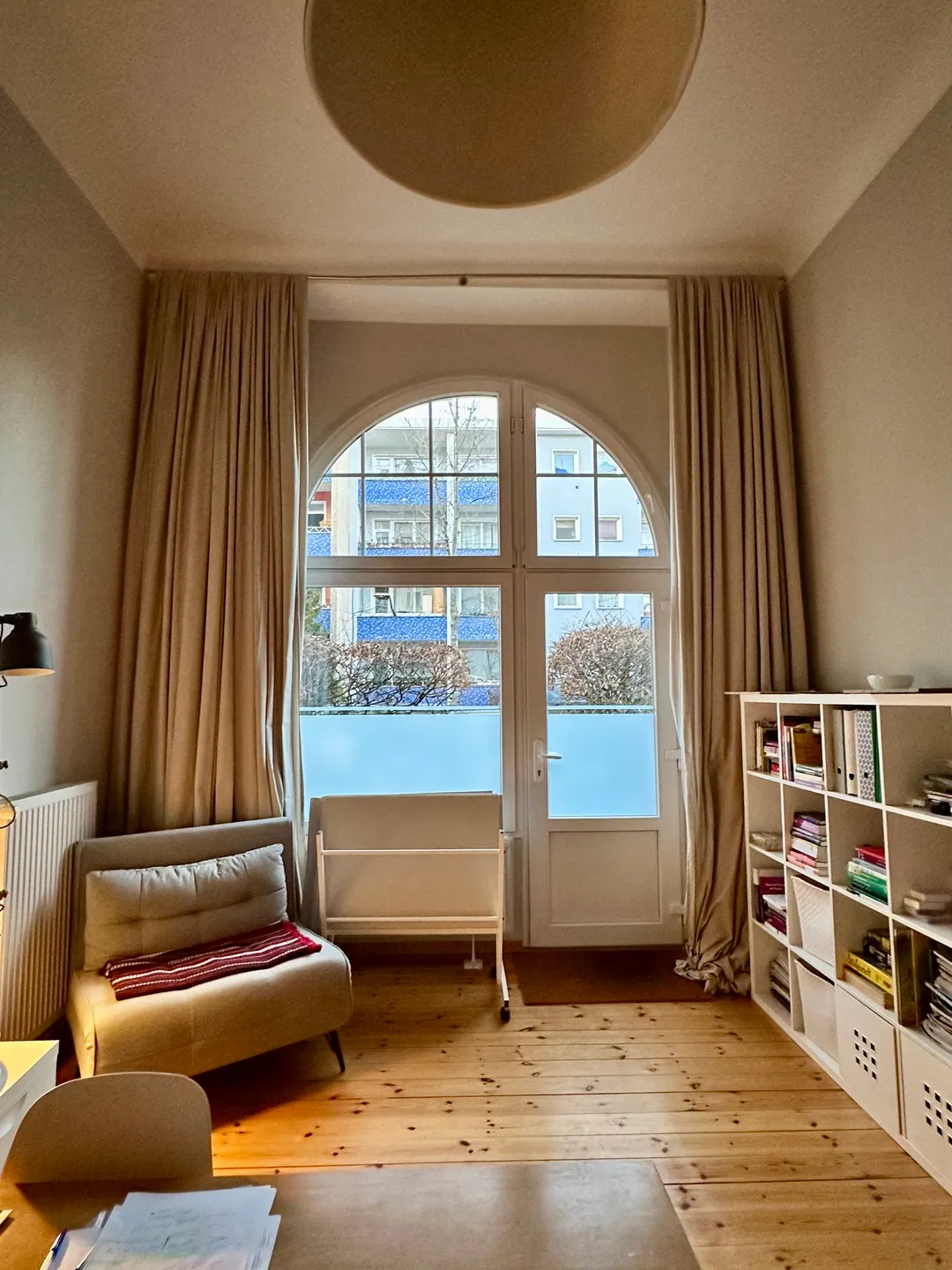 Ein Therapieraum mit Rundbogenfenster, Dielenboden, Sessel und einem Regal mit Ordnern und Büchern